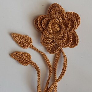 May include: A crocheted flower with two leaves and a long stem in a brown color.