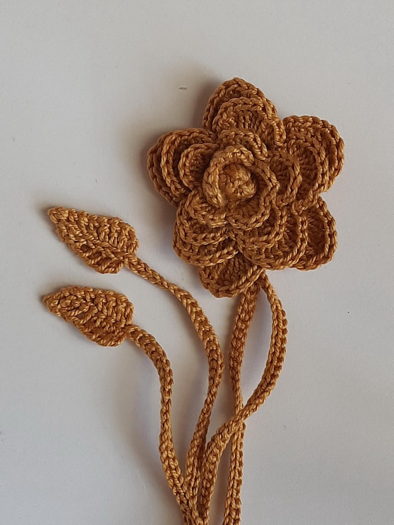 May include: A crocheted flower with two leaves and a long stem in a brown color.