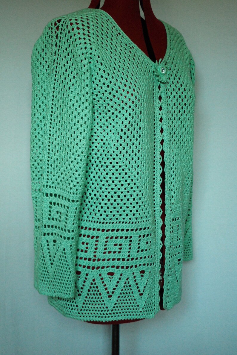 May include: A light green crocheted cardigan with a button fastening. The cardigan features a delicate, lacy pattern and a scalloped edge.