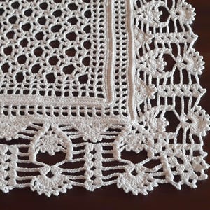 May include: White crocheted doily with a square center and a decorative border. The doily has a delicate, intricate design.