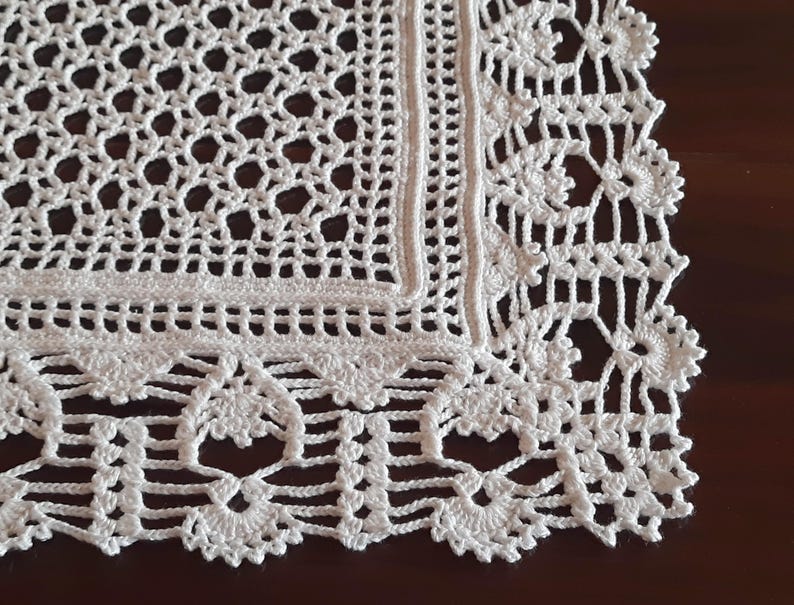 May include: White crocheted doily with a square center and a decorative border. The doily has a delicate, intricate design.
