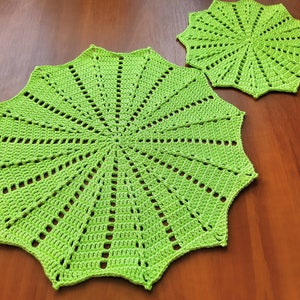 May include: Two green crocheted doilies with a starburst pattern. The larger doily is 12 inches in diameter and the smaller doily is 8 inches in diameter.