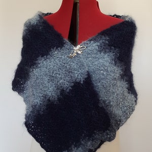 May include: A blue and gray knitted shawl with a decorative pin. The shawl is made of a soft, fluffy yarn and has a loose, drapey style.