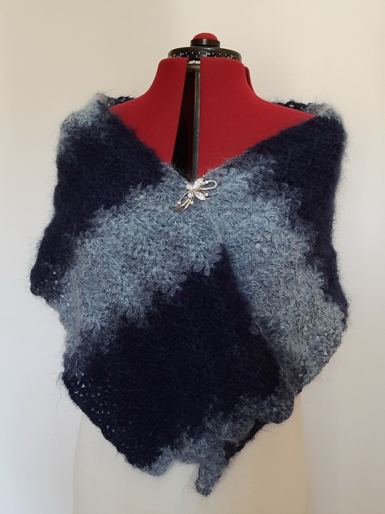 May include: A blue and gray knitted shawl with a decorative pin. The shawl is made of a soft, fluffy yarn and has a loose, drapey style.