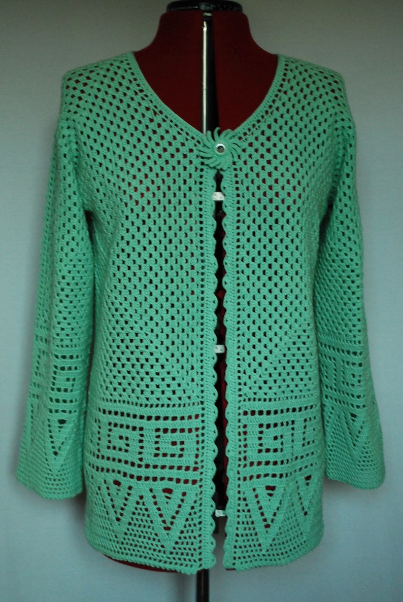 May include: A green crocheted cardigan with a button fastening and a scalloped hem. The cardigan features a geometric pattern and is made from a lightweight yarn.