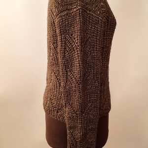 May include: A brown knitted sweater with a cable knit pattern. The sweater is on a dress form.