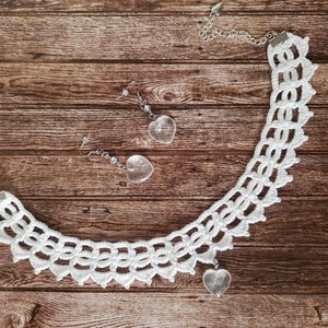 May include: White crocheted necklace with a heart-shaped crystal pendant. Matching heart-shaped crystal earrings are also included.