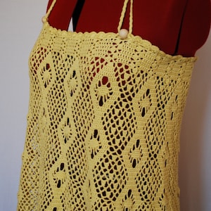 May include: A yellow crochet dress with a delicate pattern and a simple design. The dress has a halter neckline and is made of a lightweight, breathable fabric.