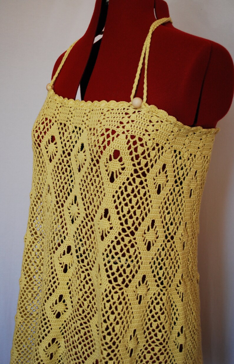 May include: A yellow crochet dress with a delicate pattern and a simple design. The dress has a halter neckline and is made of a lightweight, breathable fabric.
