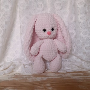 K&ouml;nnte beinhalten: Ein rosa geh&auml;keltes Hasenspielzeug mit schwarzen Augen und einer rosa Nase. Der Hase sitzt auf einem wei&szlig;en Spitzenstoff-Hintergrund.