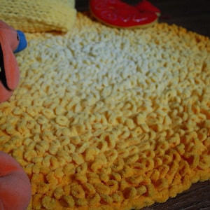 May include: A yellow and white crocheted rug with a gradient pattern. The rug is made of soft, fluffy yarn and has a round shape.