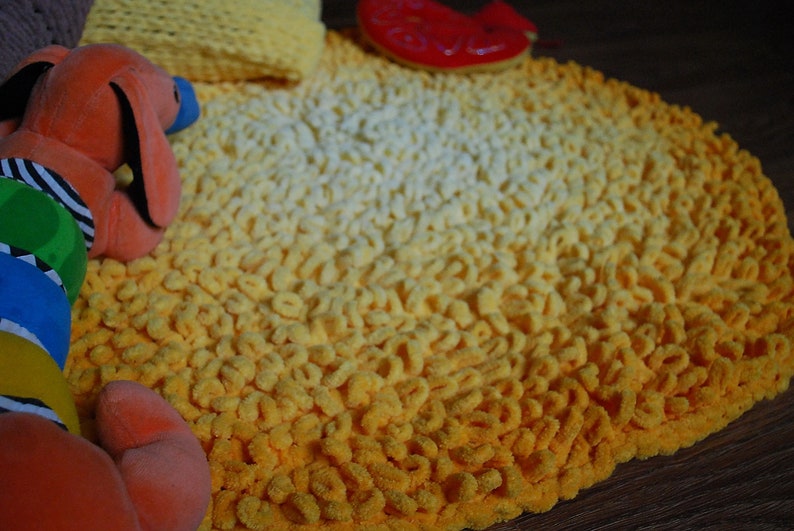 May include: A yellow and white crocheted rug with a gradient pattern. The rug is made of soft, fluffy yarn and has a round shape.