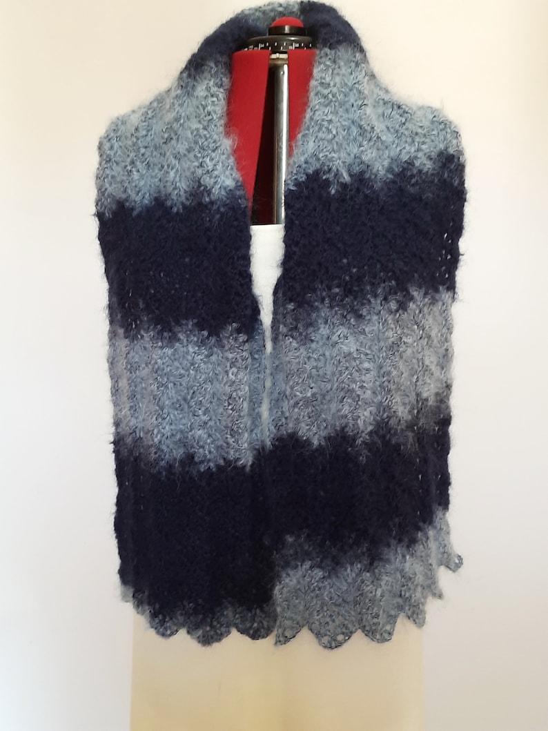 May include: A blue and gray striped knitted scarf with a scalloped edge.