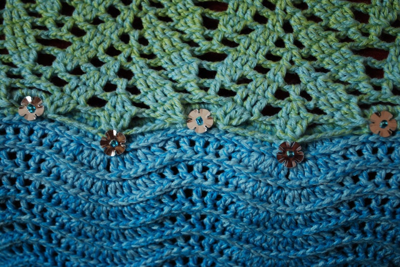May include: A crocheted shawl with a green and blue ombre pattern. The shawl is decorated with silver flower-shaped embellishments.