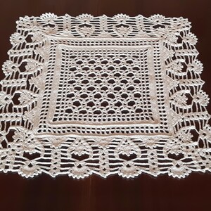 May include: White crocheted doily with a square center and a decorative border. The doily is made of delicate, intricate stitches.
