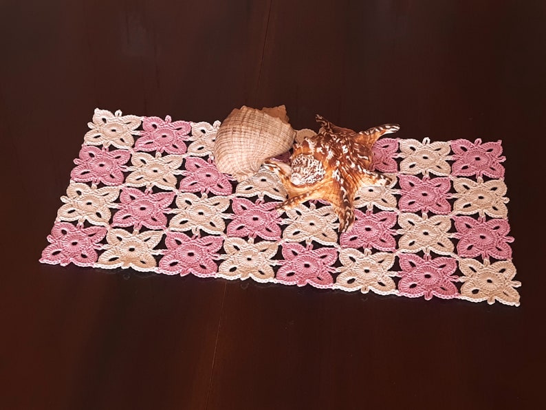May include: A pink and cream crocheted doily with two seashells on top.