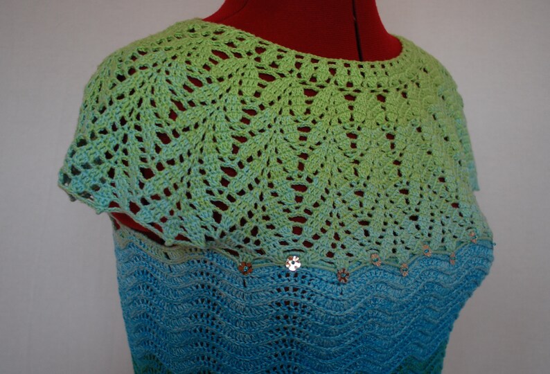May include: A crocheted top with a green and blue ombre design. The top has a scalloped neckline and is decorated with sequins.