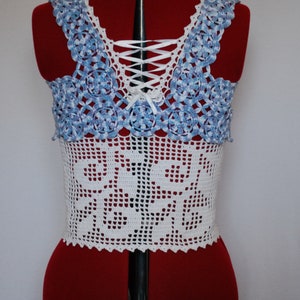 Puede incluir: Top blanco de crochet con un dise&ntilde;o de patr&oacute;n azul y blanco. El top tiene una espalda con cordones con una cinta blanca.