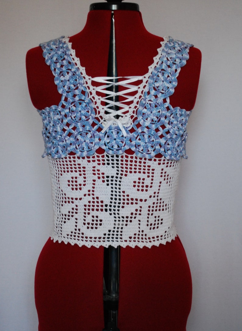 Puede incluir: Top blanco de crochet con un dise&ntilde;o de patr&oacute;n azul y blanco. El top tiene una espalda con cordones con una cinta blanca.