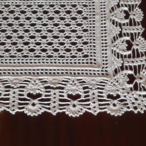 K&ouml;nnte beinhalten: Wei&szlig;e H&auml;keltischdecke mit quadratischem Mittelteil und einem gewellten Rand. Die Tischdecke hat ein zartes Blumenmuster.