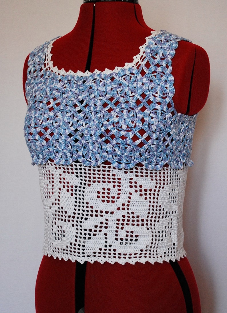 Puede incluir: Un top blanco de ganchillo sin mangas con un dise&ntilde;o de ganchillo azul y blanco en la parte superior. El top est&aacute; en un maniqu&iacute; rojo.