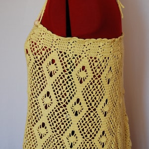 May include: A yellow crochet top with a delicate pattern. The top has a halter style with a tie at the back.