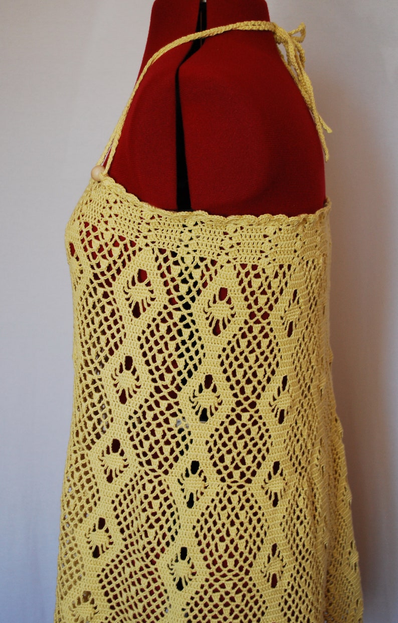 May include: A yellow crochet top with a delicate pattern. The top has a halter style with a tie at the back.