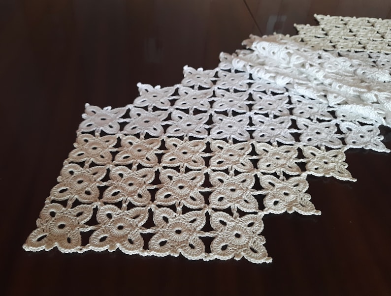 May include: White crocheted table runner with a delicate floral pattern. The runner is made of a fine thread and has a scalloped edge.