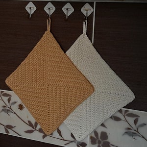 May include: Two crocheted pot holders hanging on hooks. One is beige and the other is white.
