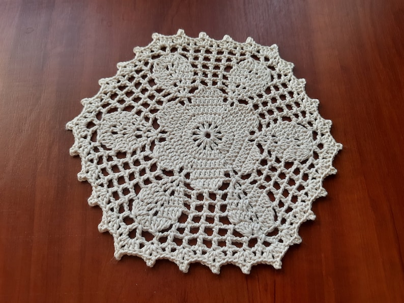 May include: A white crocheted doily with a delicate floral design. The doily is circular and has a scalloped edge.