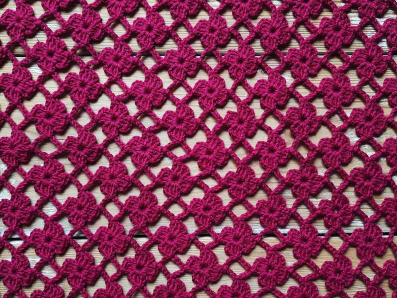 Puede incluir: Primer plano de un encaje de ganchillo con un patr&oacute;n repetitivo de flores burdeos. El encaje est&aacute; hecho con un hilo fino y tiene un aspecto delicado y de encaje.