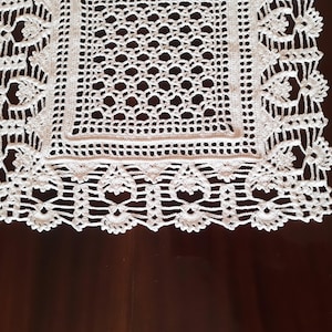 May include: White crocheted table runner with a square center and a delicate lace border.