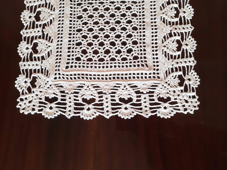 May include: White crocheted table runner with a square center and a delicate lace border.