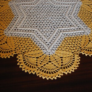 May include: A white crocheted tablecloth with a yellow crocheted border. The tablecloth features a star design in the centre.