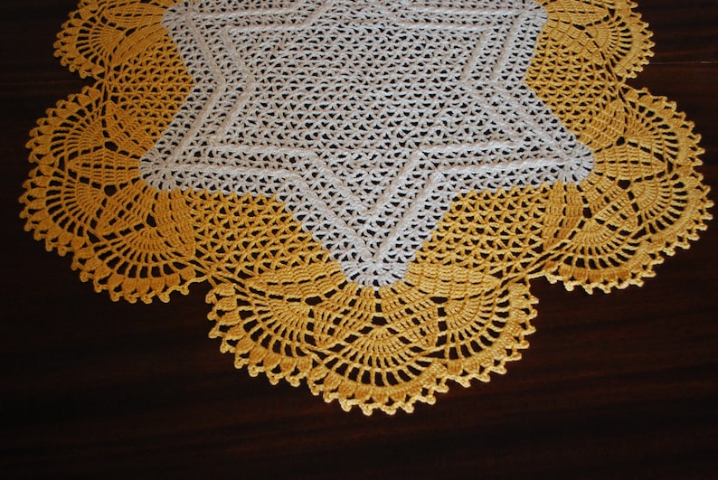 May include: A white crocheted tablecloth with a yellow crocheted border. The tablecloth features a star design in the centre.