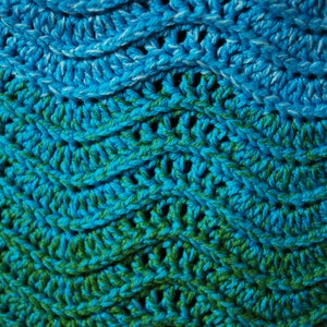 May include: Close-up of a crocheted fabric with a gradient of blue and green colors. The fabric has a textured, woven pattern.