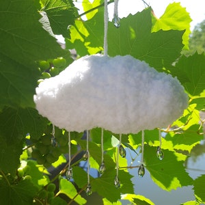 Puede incluir: Adorno en forma de nube blanca y esponjosa con l&aacute;grimas de cristal colgantes. La nube est&aacute; suspendida por una cuerda blanca, sobre un fondo de hojas verdes de vid y luz solar. Un art&iacute;culo decorativo caprichoso.