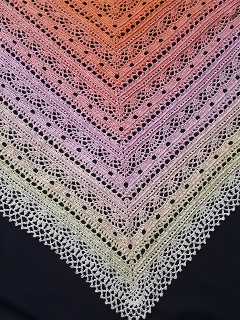 May include: A handmade crochet shawl with a gradient of colors, transitioning from peach to pink and finally to a cream-colored border. The shawl features an open, lacy design with a scalloped edge, perfect for adding a touch of elegance to any outfit.