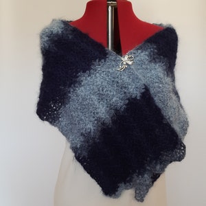 May include: A blue and gray knitted shawl with a decorative pin on a white dress form.