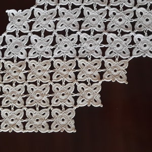 May include: White crocheted table runner with a geometric pattern of flowers. The runner has a scalloped edge and is made of delicate, intricate stitches.