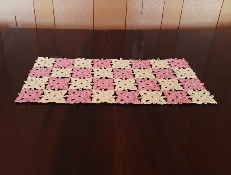 May include: A crocheted table runner with a pink and cream butterfly design.