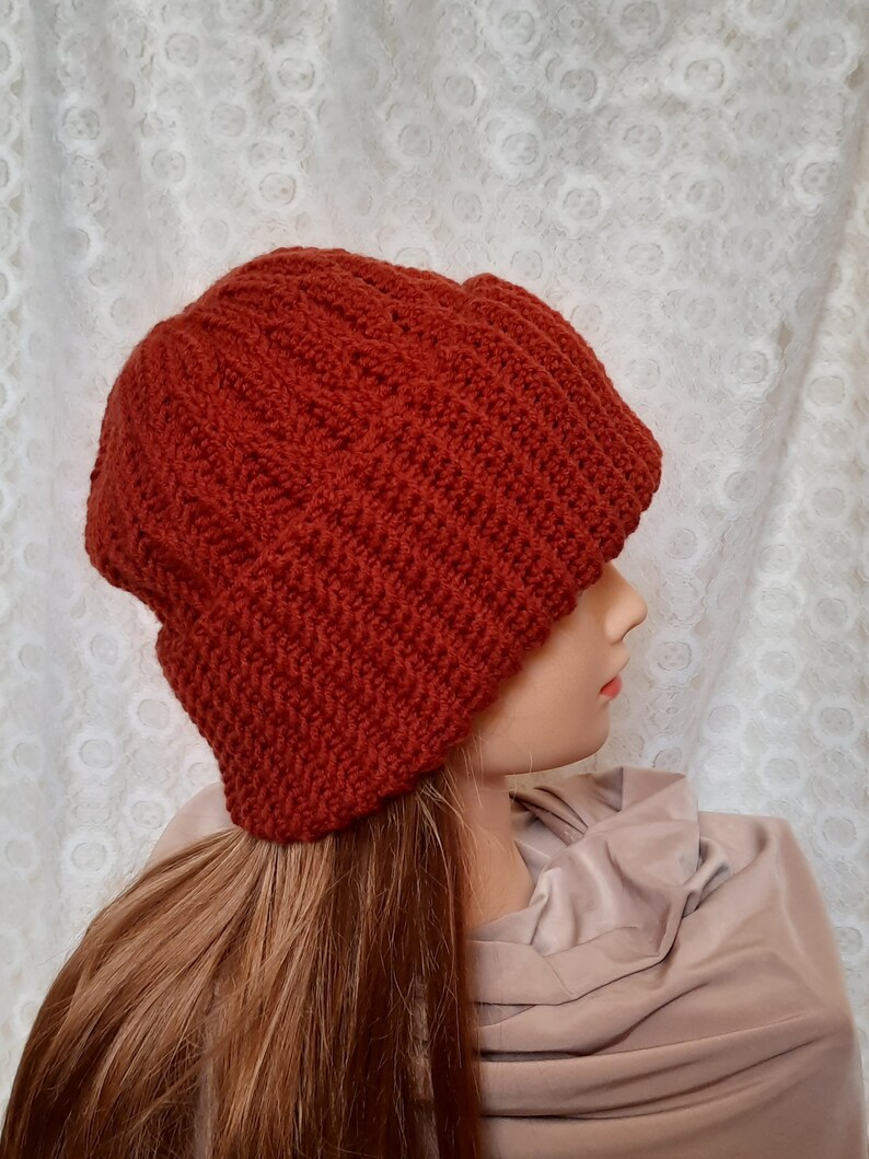 May include: A rust-colored knitted beanie hat with a slouchy fit. The hat is made of a soft, textured yarn.