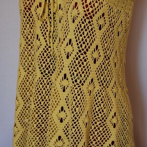 May include: A yellow crochet dress with a delicate pattern and a tie at the neckline.