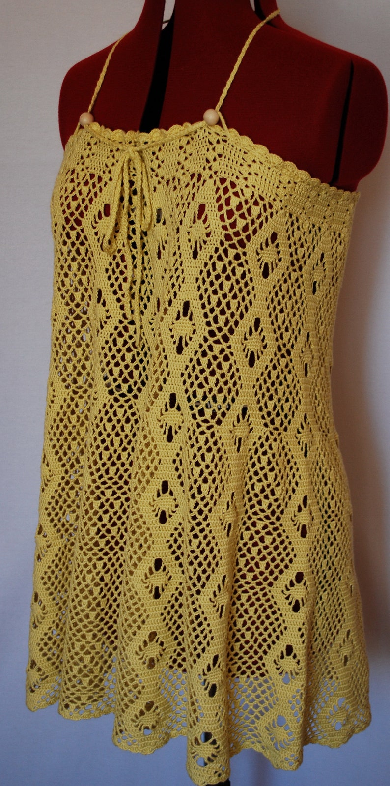 May include: A yellow crochet dress with a delicate pattern and a tie at the neckline.