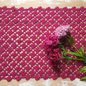Puede incluir: Un encaje de ganchillo rosa con un delicado patr&oacute;n floral, con un ramo de claveles rosas y blancos.
