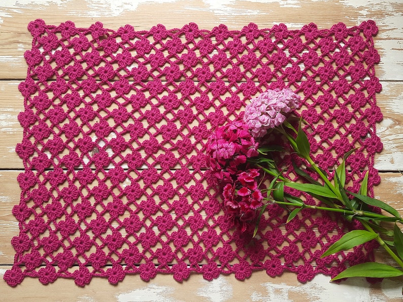 Puede incluir: Un encaje de ganchillo rosa con un delicado patr&oacute;n floral, con un ramo de claveles rosas y blancos.