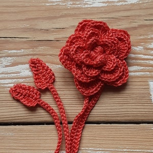 May include: A crocheted red flower with three stems and leaves. The flower is made of multiple layers of crocheted circles.