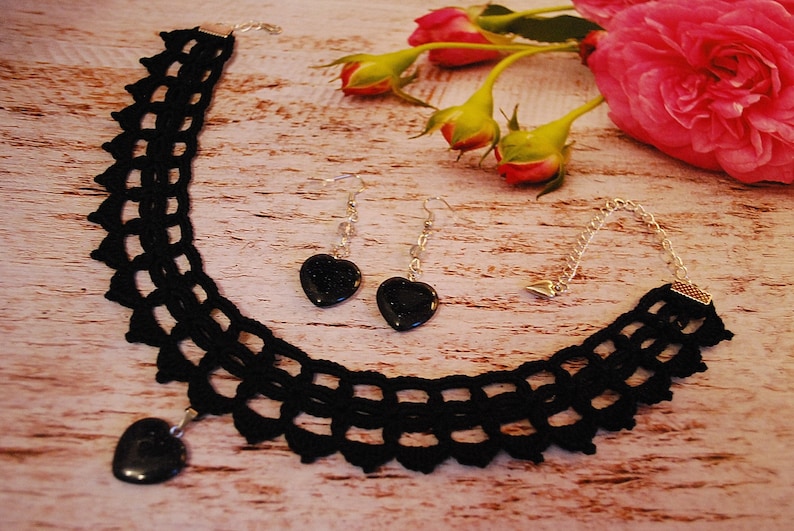 May include: A black crocheted choker necklace with a heart-shaped pendant and matching earrings. The pendant and earrings feature black heart-shaped stones.