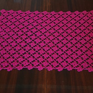 Puede incluir: Un camino de mesa de ganchillo rosa con un patr&oacute;n floral.