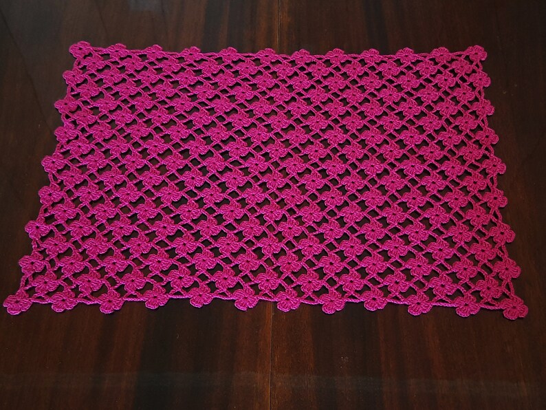 Puede incluir: Un camino de mesa de ganchillo rosa con un patr&oacute;n floral.